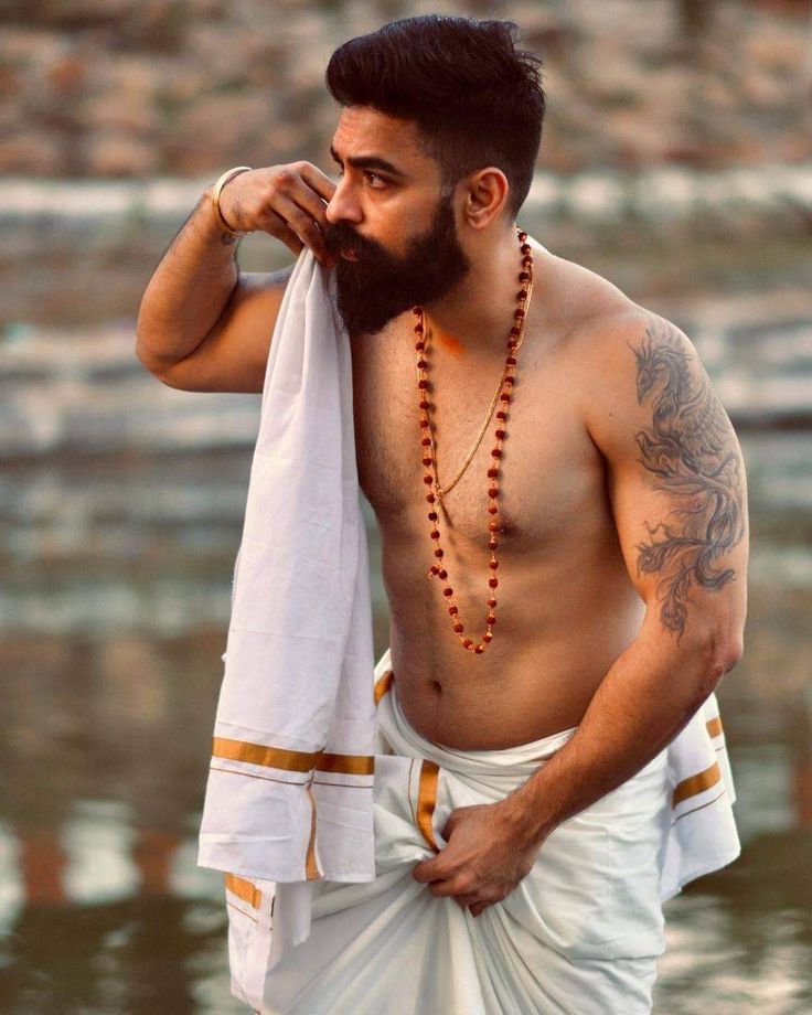 a man with tattoos on his chest wearing a white sari and beads around his neck