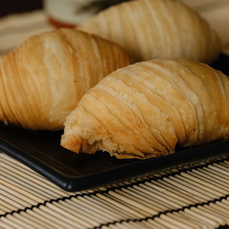 two croissants on a black plate sitting on a bamboo mat with a cup in the background