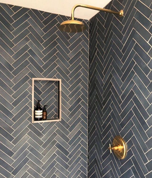 a bathroom shower with herringbone tile and gold fixtures