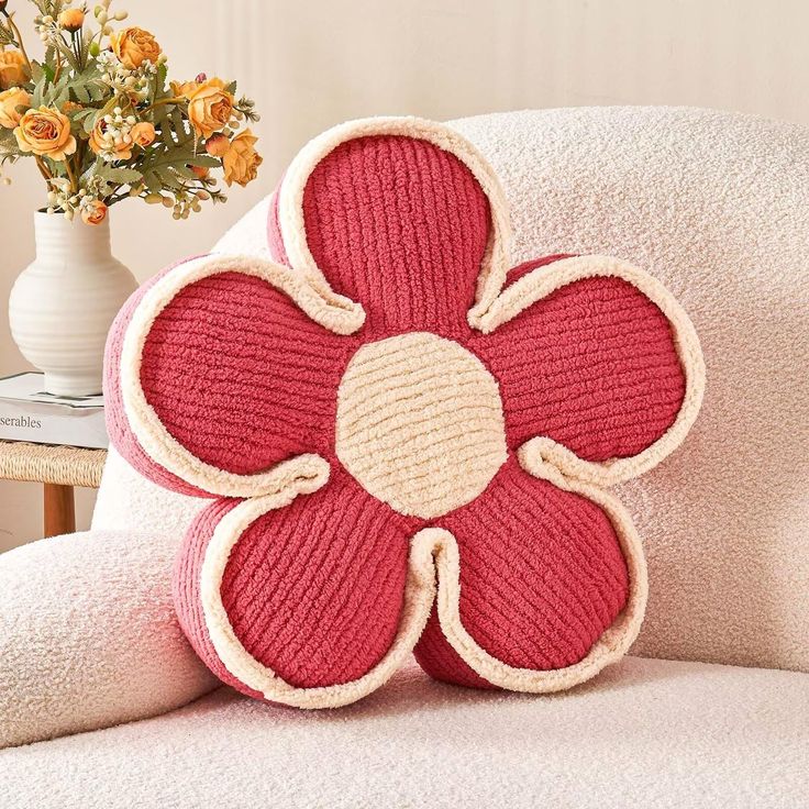 a red flower pillow sitting on top of a white chair next to a vase with yellow flowers