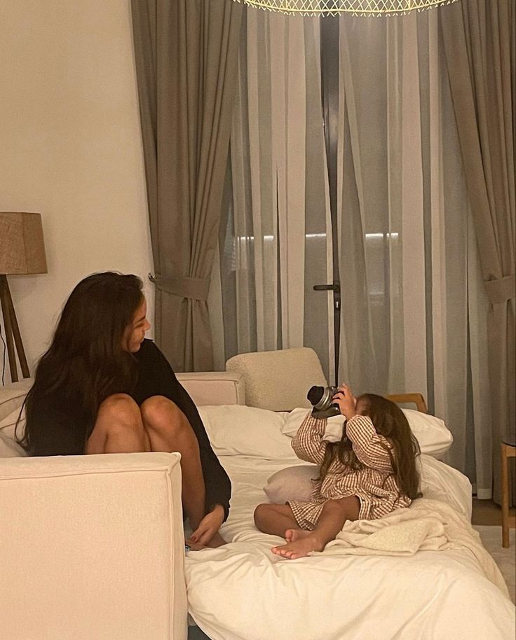 two women are sitting on a bed and one is taking a photo with her camera