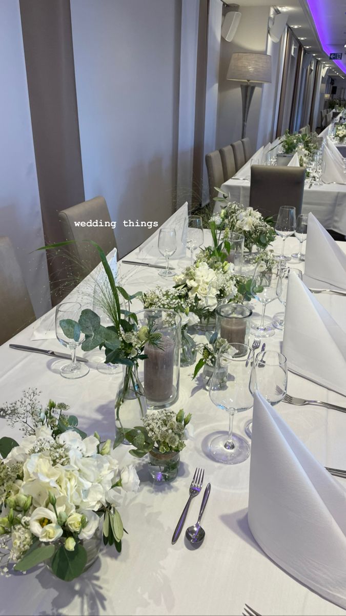 a long table is set with white flowers and place settings for the guests to sit at