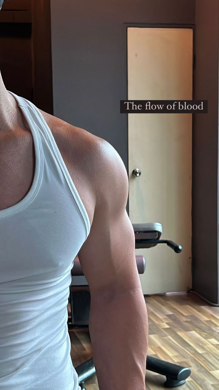 a man in white tank top standing next to a gym machine