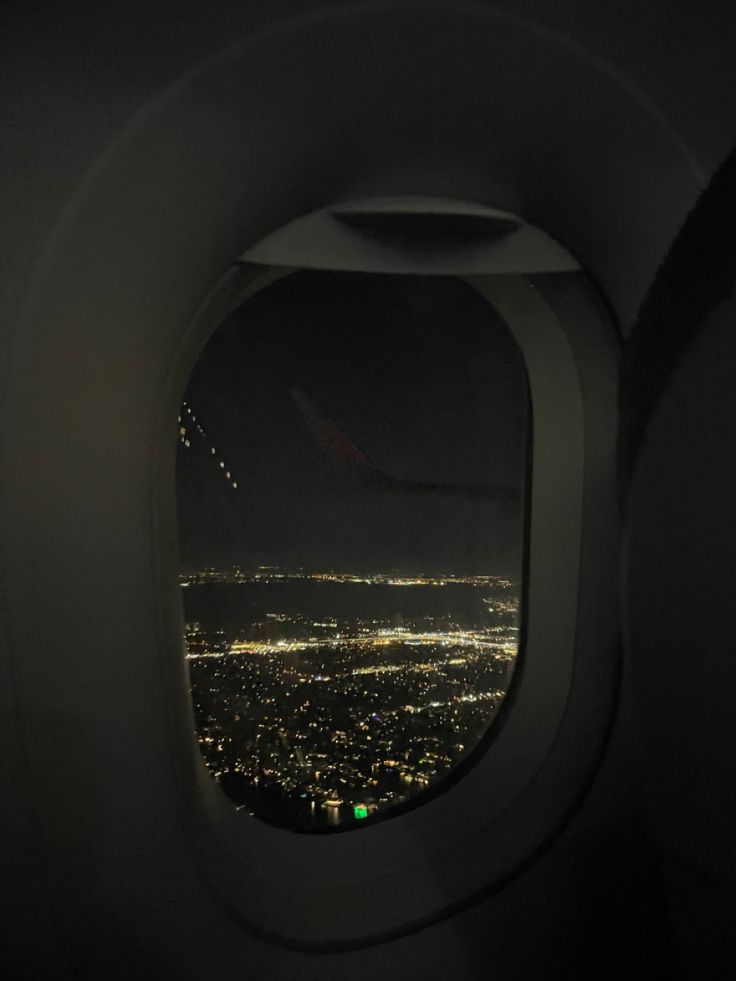 an airplane window with the view of city lights at night from it's wing