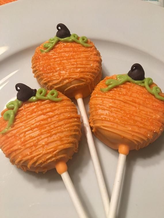 three orange cake pops on a white plate with green and black icing, sitting next to each other