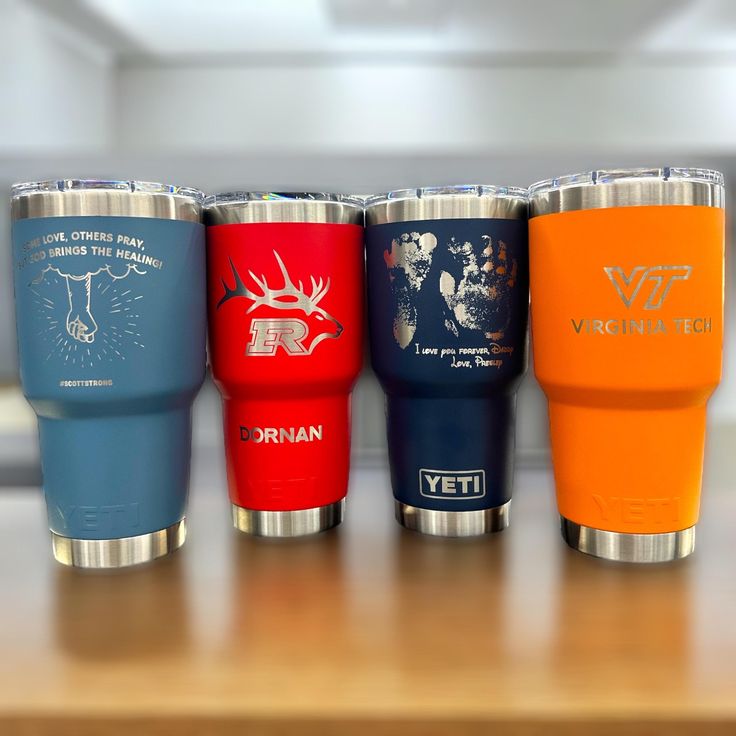 four different colored tumblers sitting on top of a wooden table next to each other