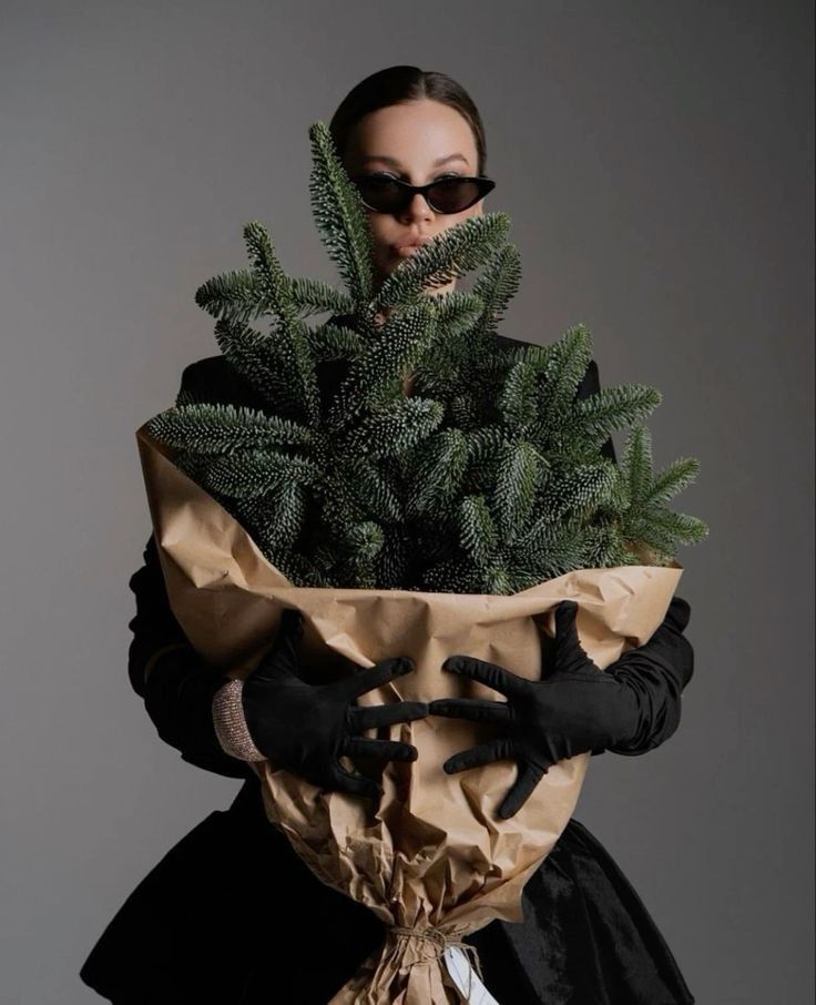 a woman in black gloves holding a brown bag filled with green plants and wearing sunglasses