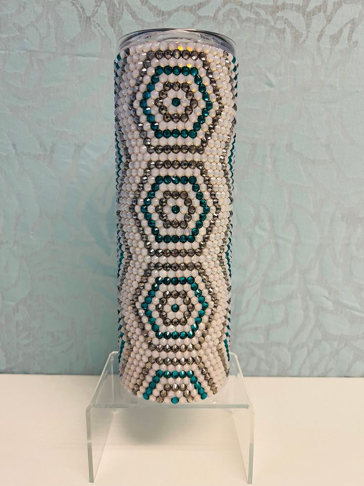 a beaded vase sitting on top of a white table next to a blue wall