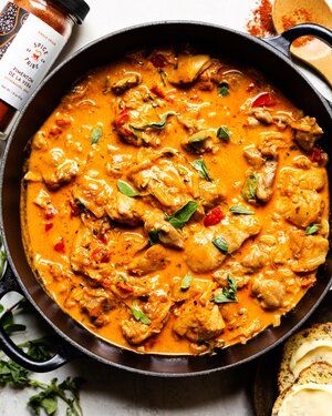 a skillet filled with chicken and vegetables on top of a white table next to bread