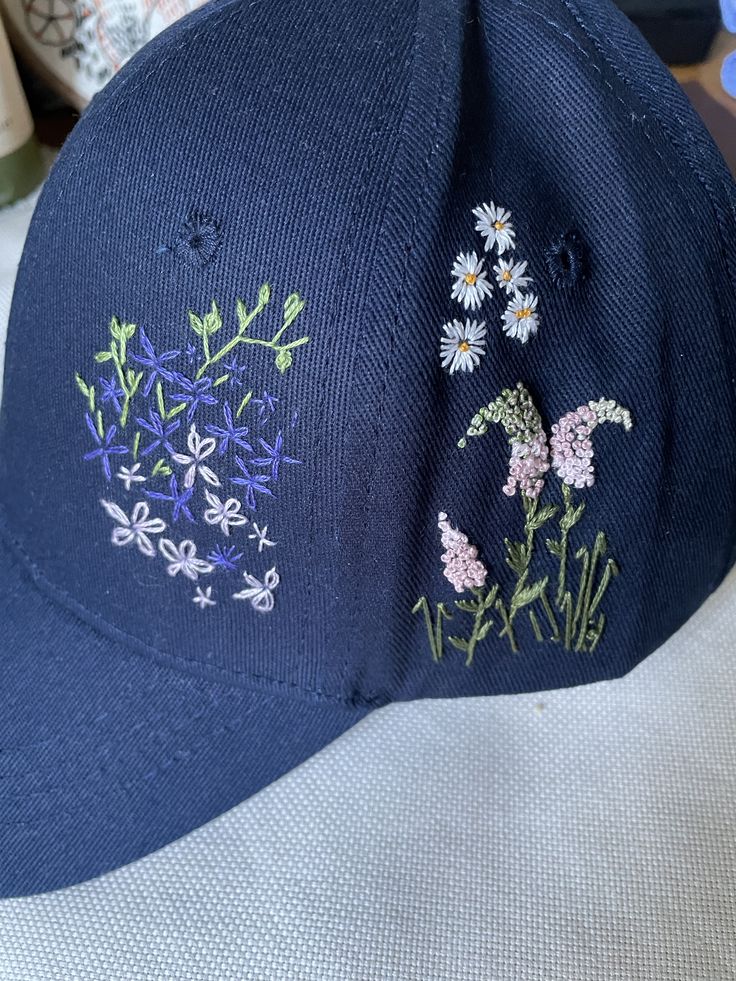 a baseball cap with embroidered flowers on it sitting on a table next to other items