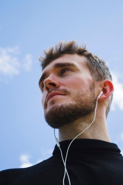 a man with ear buds on his ears looking up at the blue sky and clouds