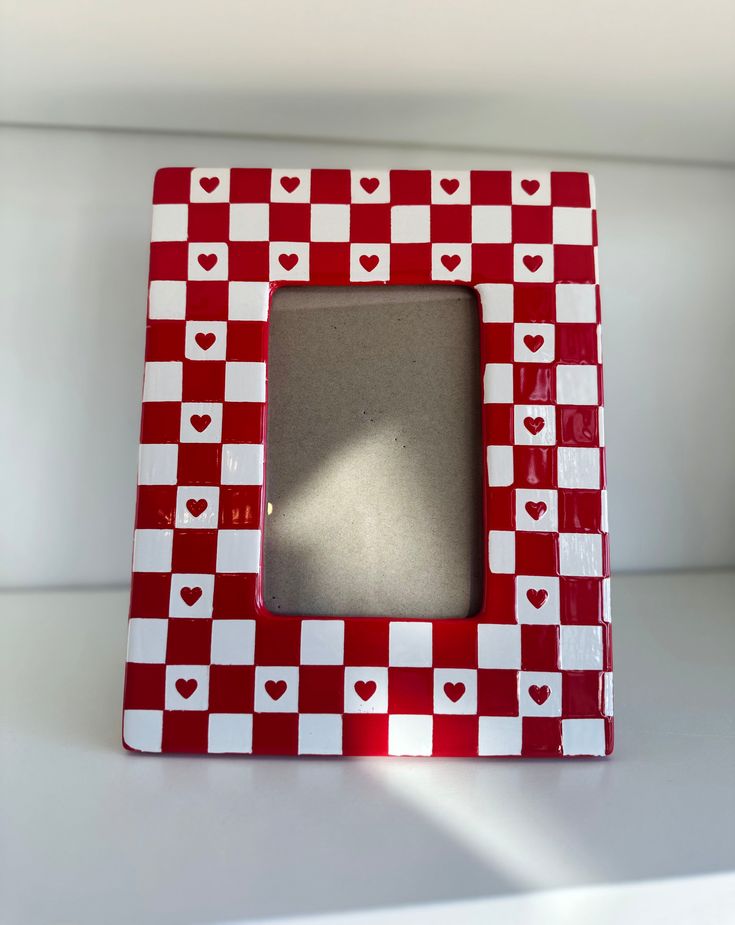 a red and white checkerboard photo frame with hearts on the front, sitting on a table