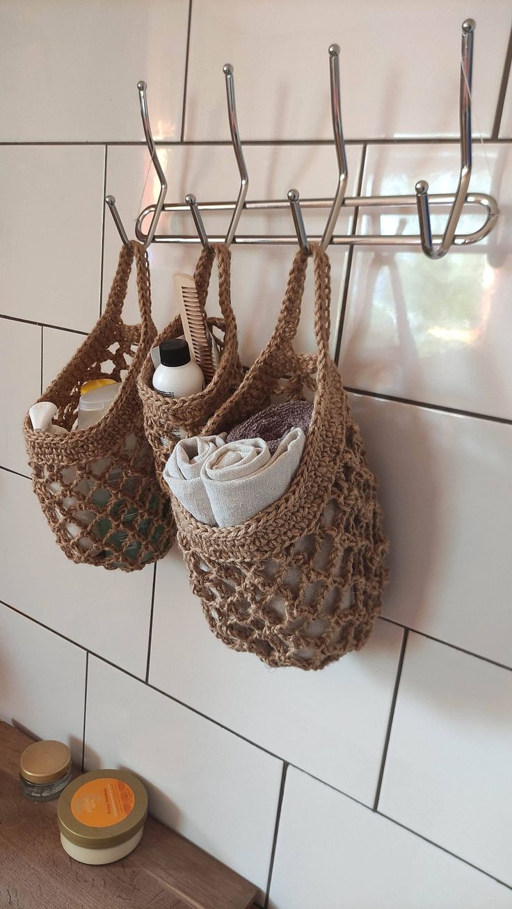 two bags hanging from hooks on a white tiled wall next to a wooden table and bowl