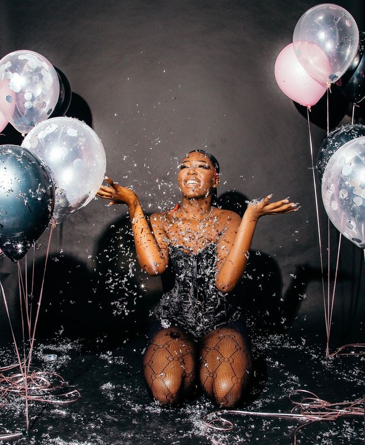 a woman sitting in the water surrounded by balloons and streaming her hands up to her face