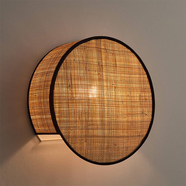 a wall light with a woven shade on it's face and the back lit