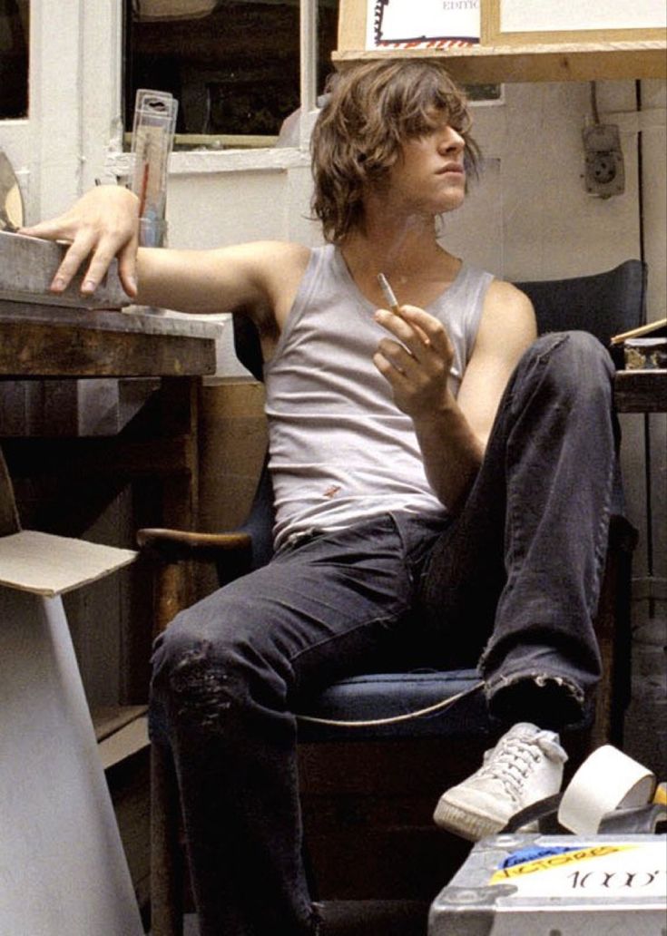 a young man sitting on top of a blue chair next to a wooden desk and shelves