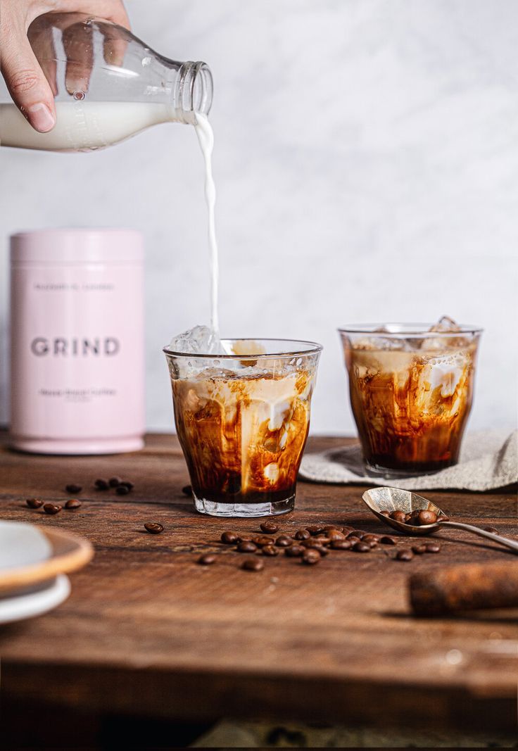 someone pouring coffee into two glasses on a wooden table