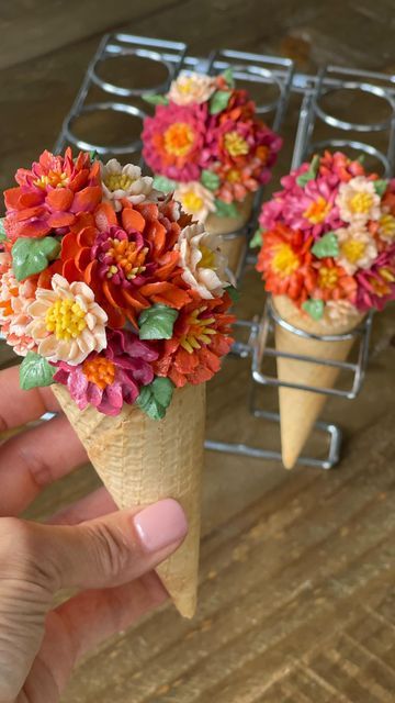 three cones filled with colorful flowers on top of a wooden table next to each other