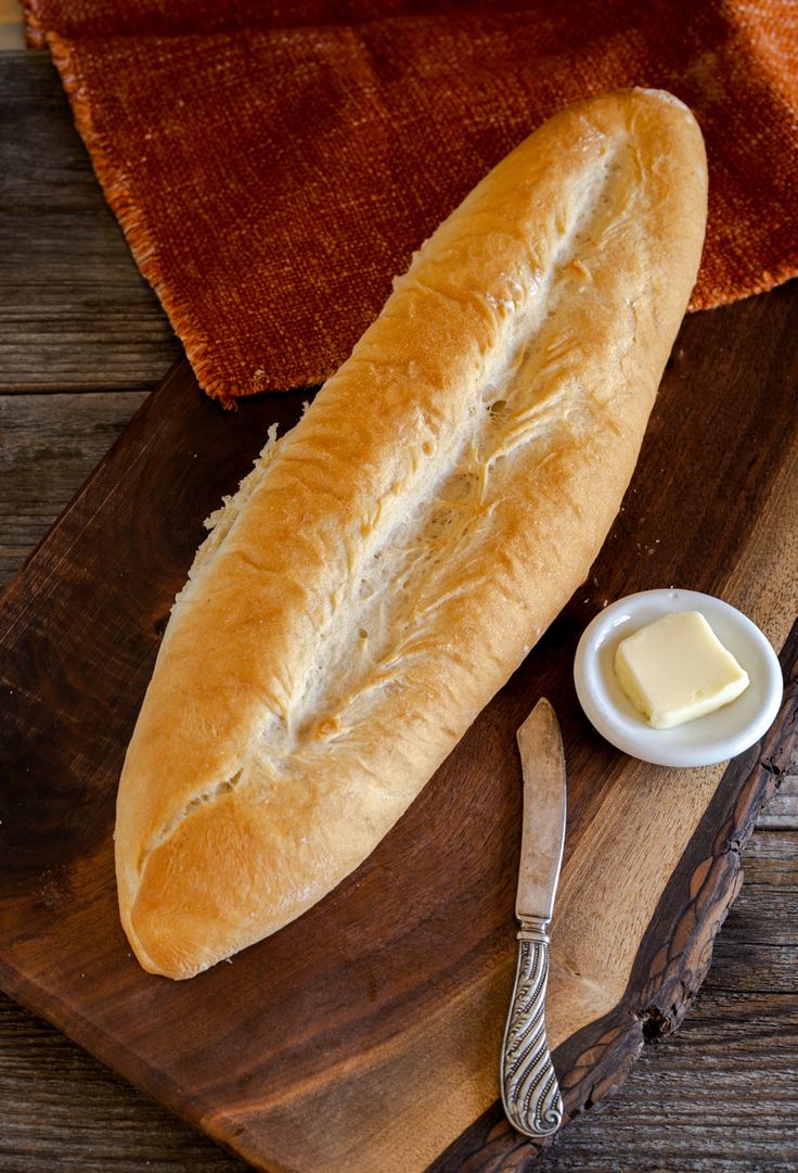 a loaf of bread sitting on top of a wooden cutting board next to butter and a knife