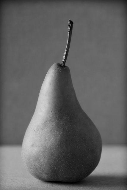 a black and white photo of a pear on a counter top with a gray background