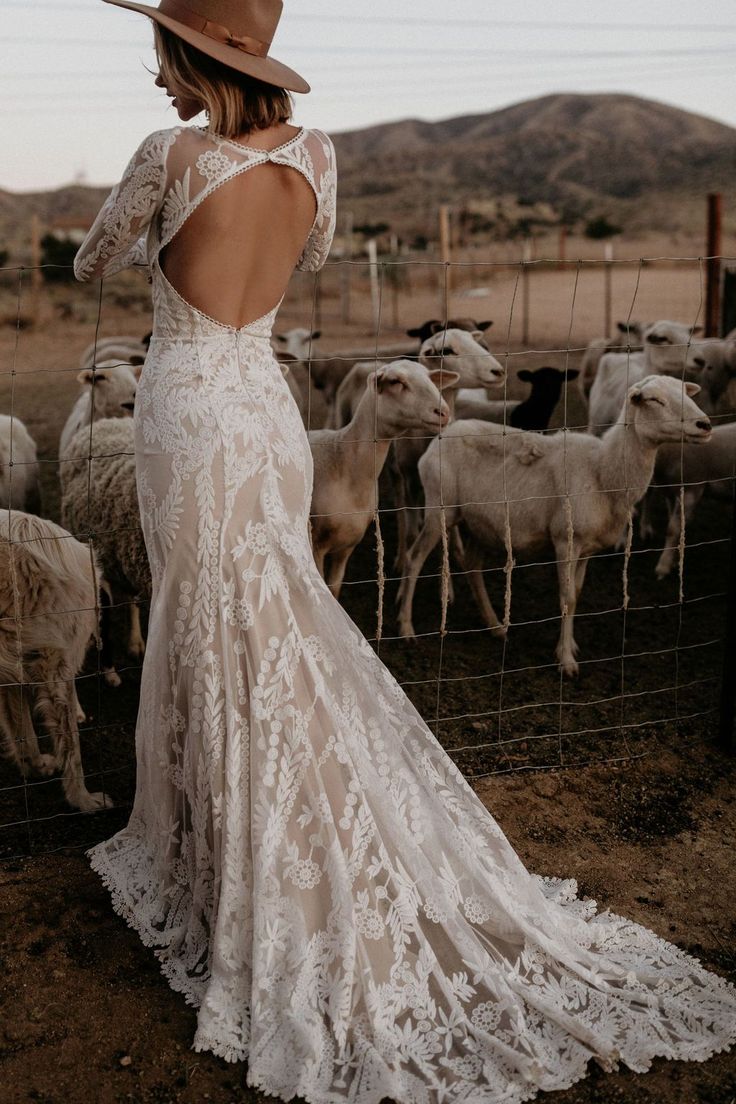 a woman standing in front of a herd of sheep wearing a white dress and hat