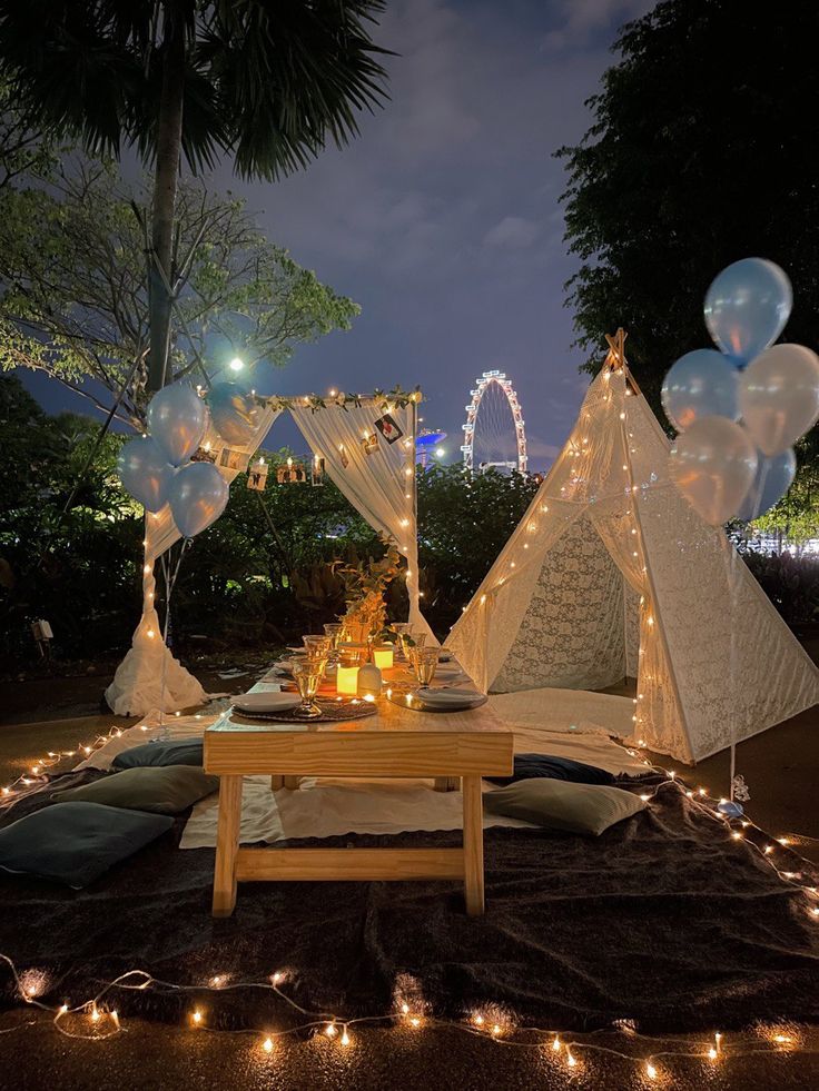 a table with balloons and lights on it in front of a teepee tent at night