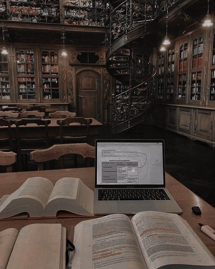 an open laptop computer sitting on top of a wooden table next to books and stairs