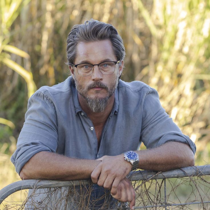 a man with glasses leaning on a fence