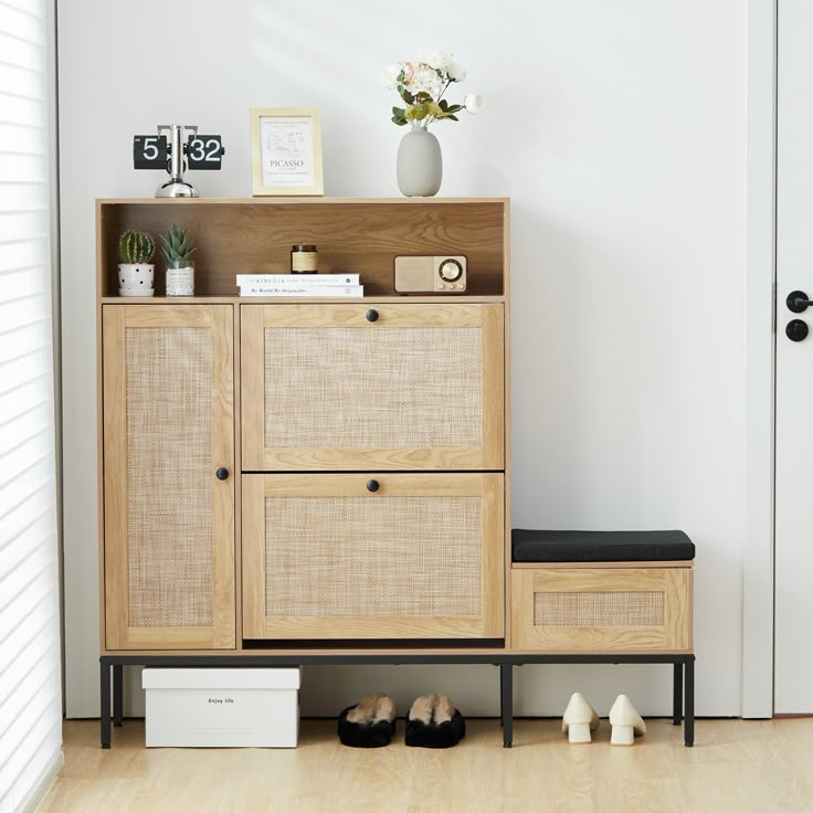 a wooden cabinet sitting next to a door with shoes on the floor and a vase filled with flowers