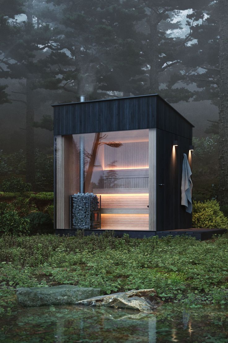 a small black cabin sitting in the middle of a forest next to a body of water