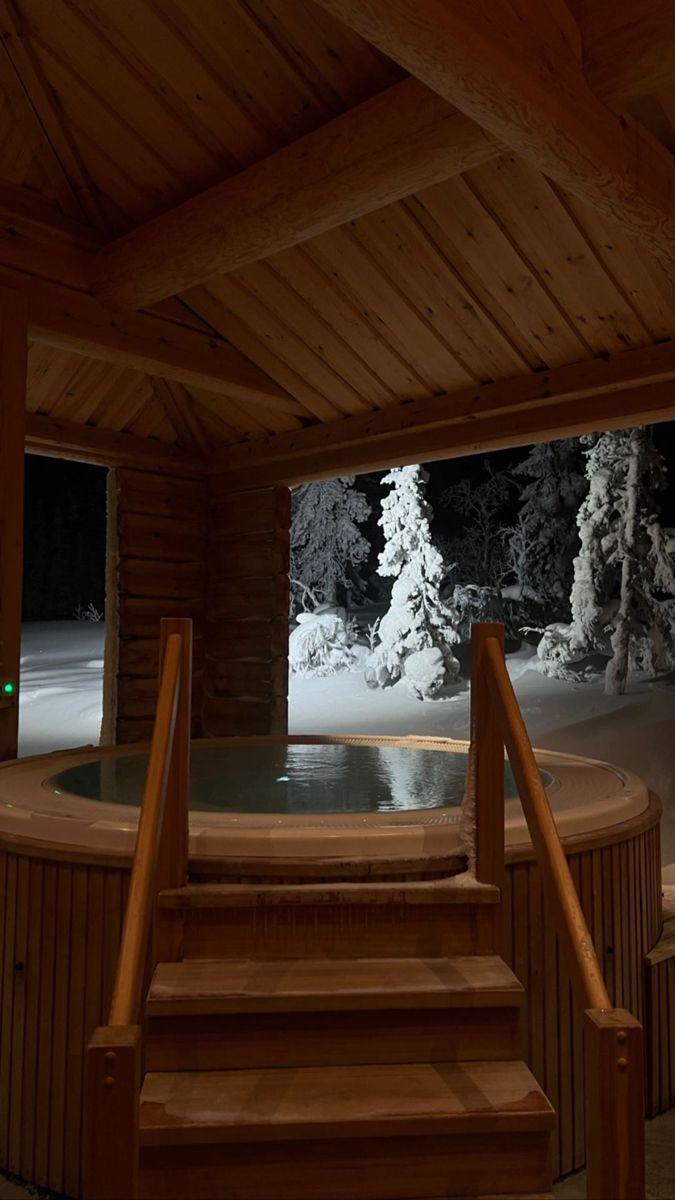 an indoor hot tub with steps leading up to it and snow covered trees in the background