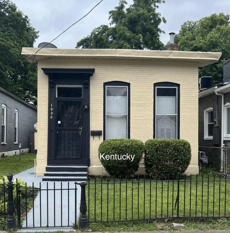 a small yellow house with a black door and fenced in yard next to it