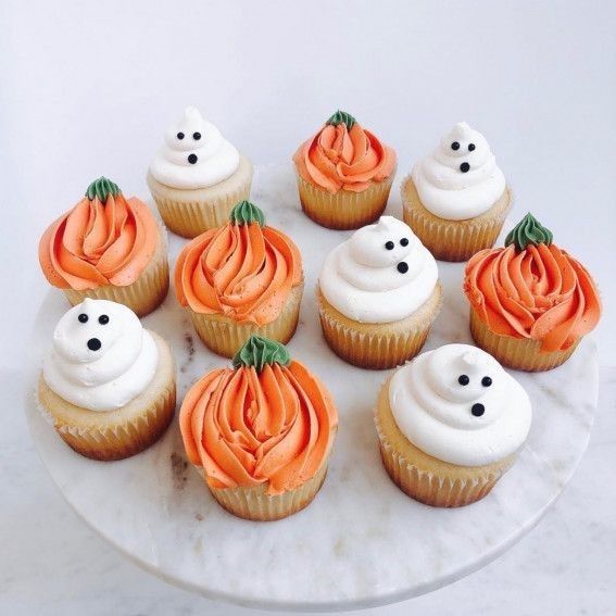 cupcakes decorated with white frosting and orange icing on a marble platter