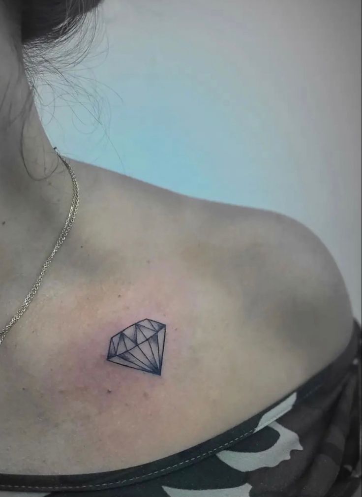 a woman's chest with a diamond tattoo on the left side of her neck