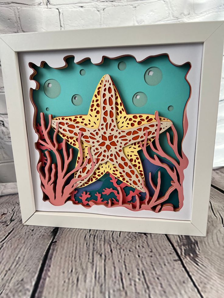 a paper cut starfish with corals and seaweed in the frame on a wooden table