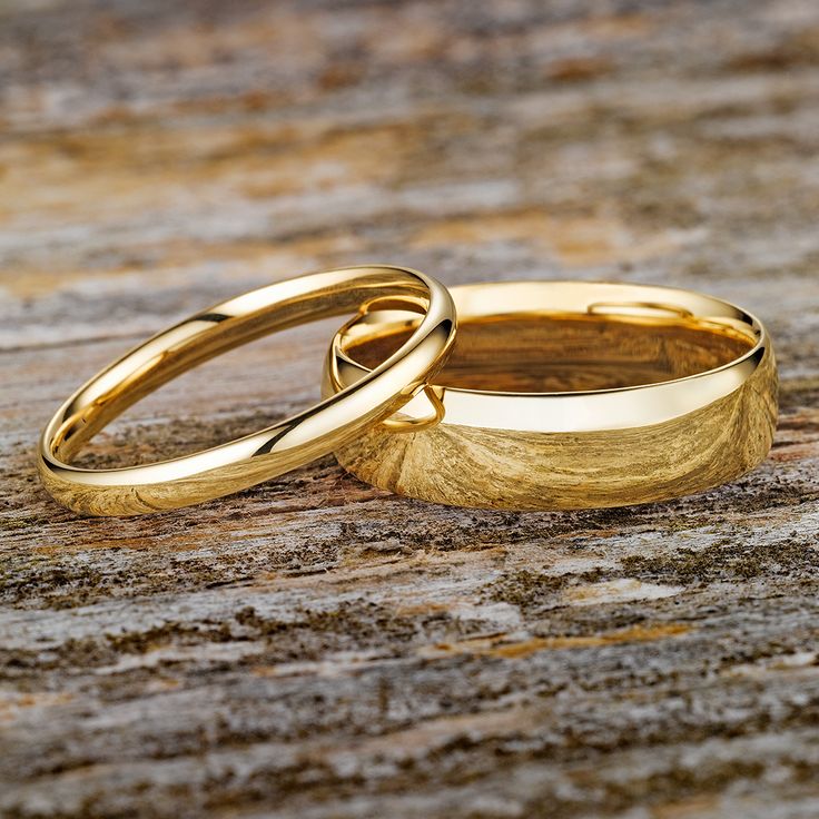 two gold wedding rings sitting on top of a piece of wood next to each other