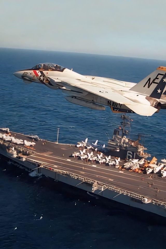 a fighter jet flying over the top of an aircraft carrier