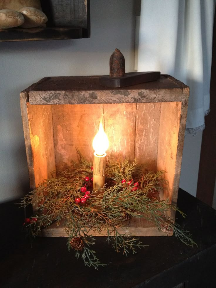 a lit candle in a wooden box sitting on a table next to a painting and window