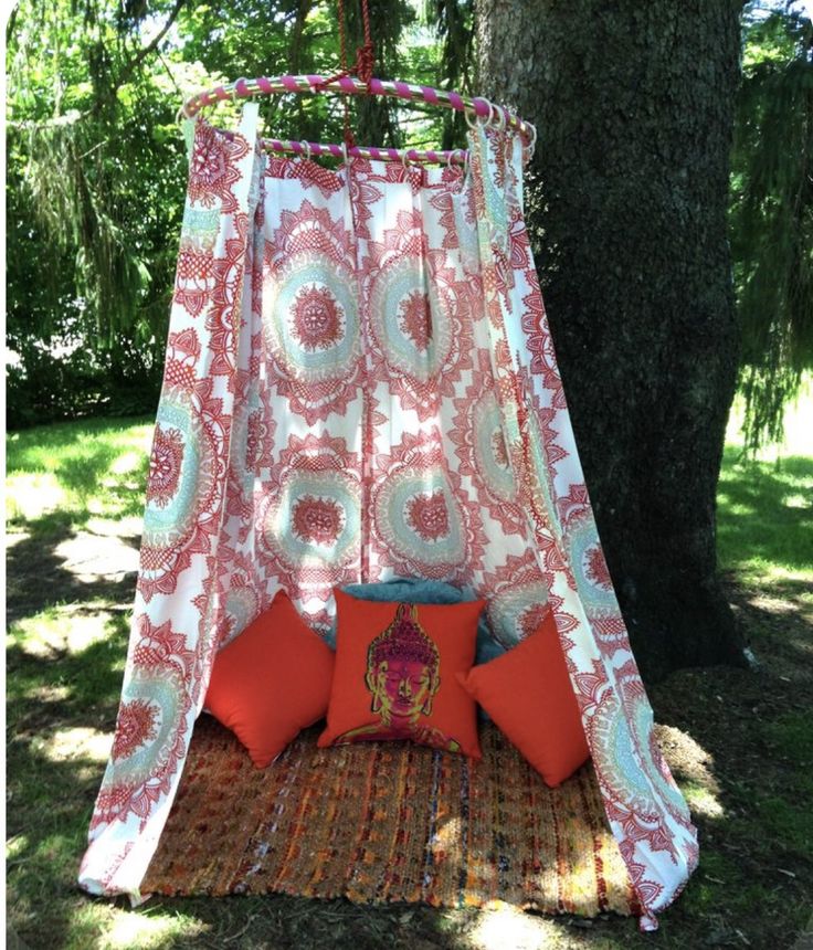 a canopy bed in the shade of a tree with red and white pillows on it