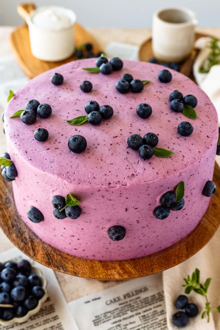 a blueberry cake on a wooden platter with fresh blueberries around the edges