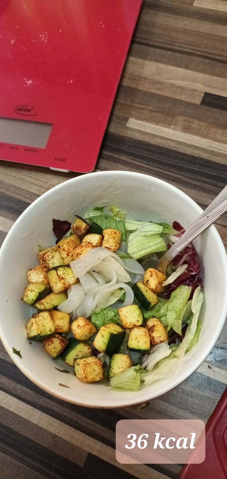 a white bowl filled with vegetables on top of a wooden table next to a red cutting board