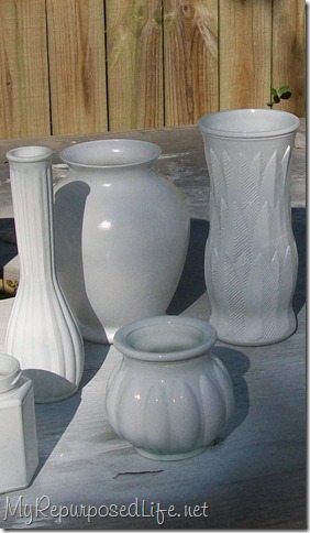 several white vases sitting on top of a table next to each other in front of a wooden fence