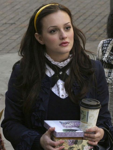 a woman is holding a coffee cup and some books in her hands while walking down the street