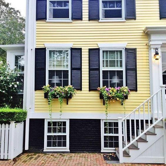 a yellow house with black shutters and flowers in the window boxes on the front