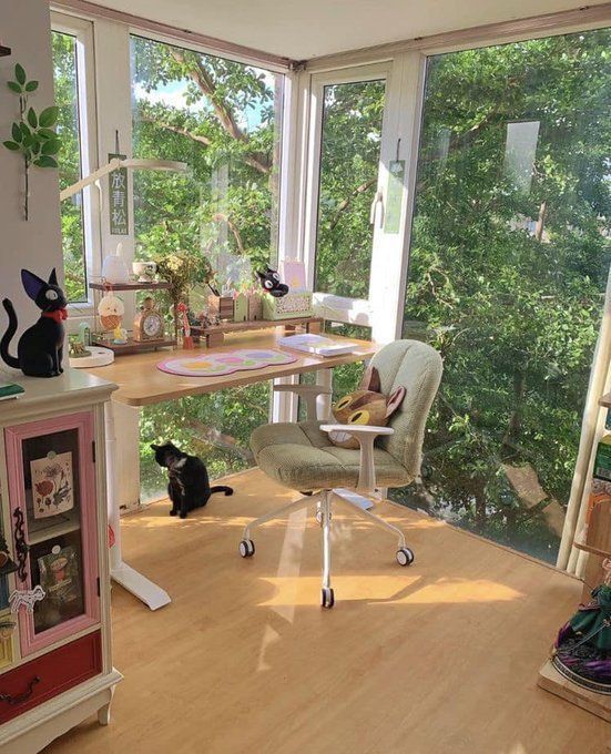 a cat sitting on top of a chair in front of a desk with a window