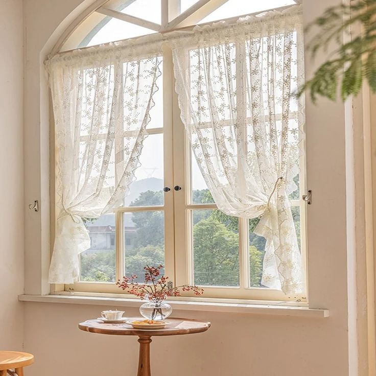 a small table and chair in front of a window with sheer curtains on the windowsill