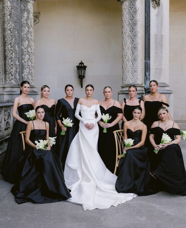 a group of women standing next to each other in black dresses and holding bouquets