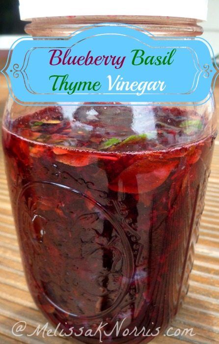 blueberry basil thyme vinegar in a jar on a wooden table with the label above it