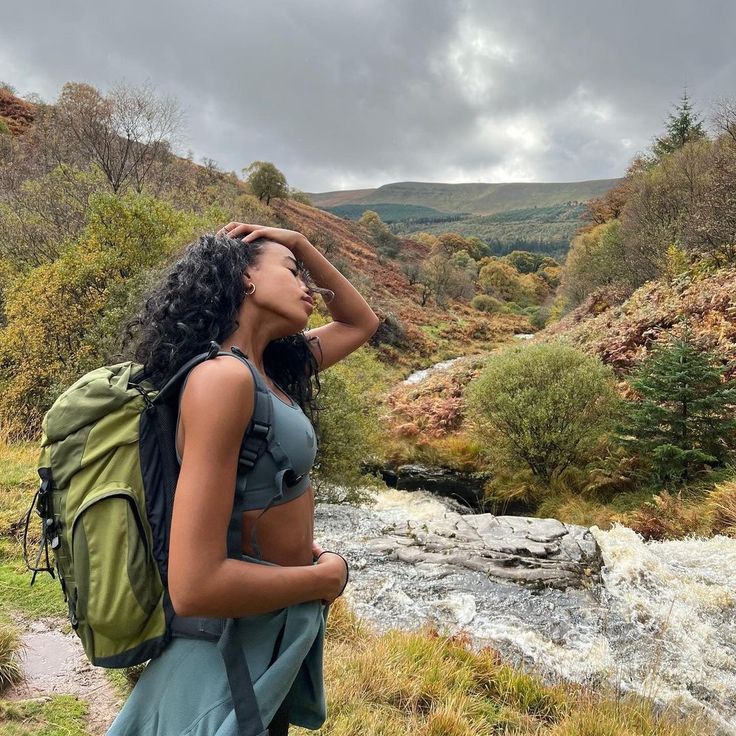 a woman with a backpack looking into the distance while standing in front of a river