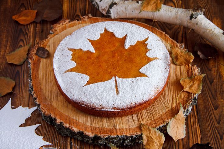 a cake decorated with a maple leaf on top of a wooden board surrounded by leaves